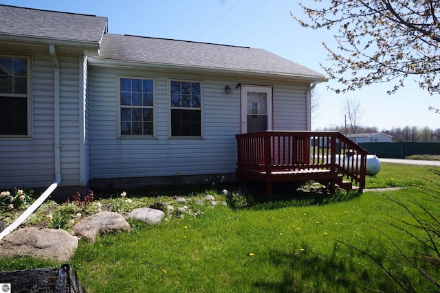 rear view of house with a yard, a wooden deck, and roof with shingles