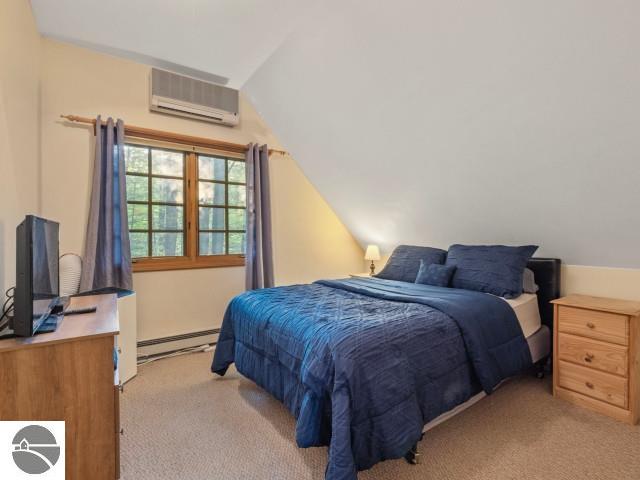 bedroom with a baseboard radiator, light colored carpet, vaulted ceiling, and a wall mounted AC