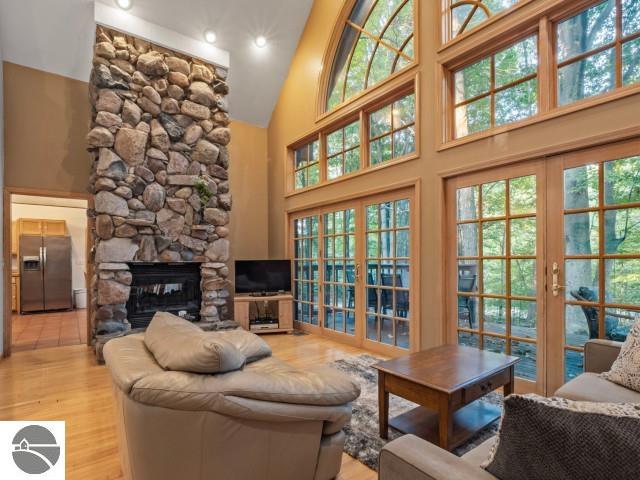 living room featuring plenty of natural light, light wood-style floors, a stone fireplace, and high vaulted ceiling