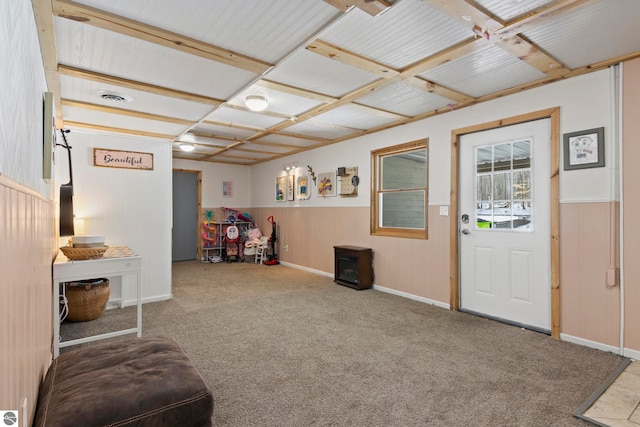 sitting room featuring a wainscoted wall, a wood stove, carpet, and visible vents