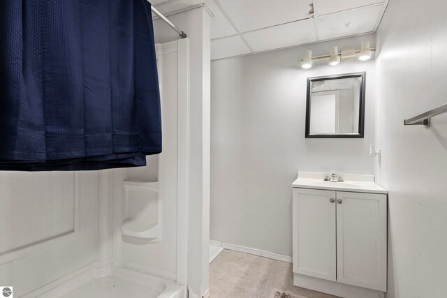 bathroom with baseboards, a drop ceiling, vanity, and walk in shower