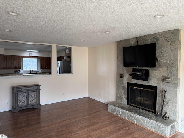unfurnished living room featuring a sink, a textured ceiling, wood finished floors, a stone fireplace, and baseboards