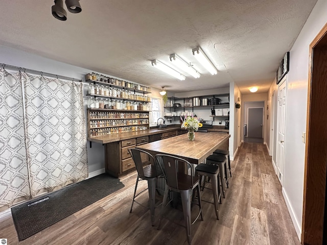 dining area with baseboards, a textured ceiling, wood finished floors, and bar area