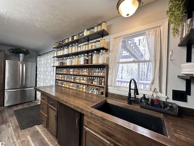 kitchen with butcher block countertops, a textured ceiling, a sink, dark wood-style floors, and freestanding refrigerator