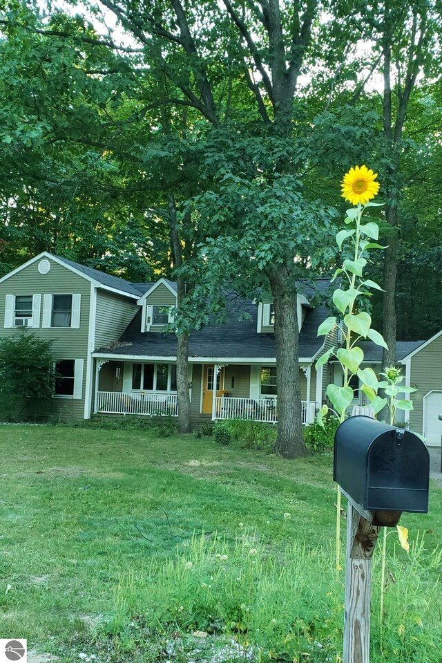 view of front of house with covered porch, roof with shingles, and a front yard