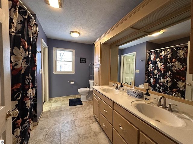 bathroom featuring double vanity, a textured ceiling, a sink, and toilet
