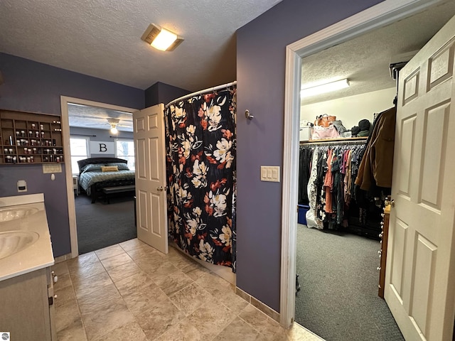 full bathroom with a spacious closet, vanity, a shower with shower curtain, and a textured ceiling