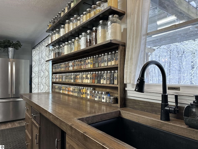 bar with a textured ceiling, wallpapered walls, a sink, a dry bar, and freestanding refrigerator