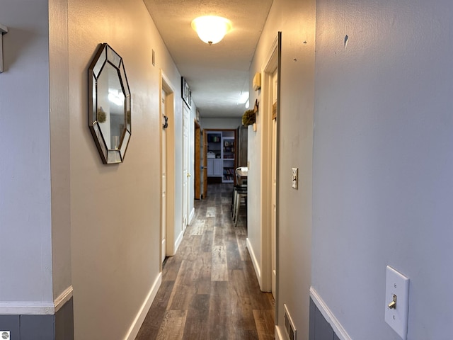 hall featuring dark wood-type flooring, baseboards, and visible vents