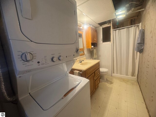 interior space featuring a sink, light floors, stacked washer and clothes dryer, laundry area, and wallpapered walls