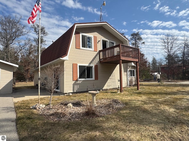 view of home's exterior with a gambrel roof, a shingled roof, a wooden deck, and a lawn