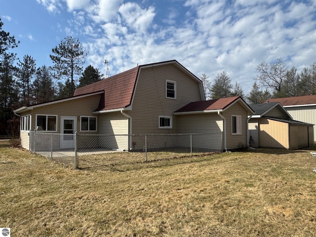 back of house featuring a gambrel roof, roof with shingles, fence, and a yard