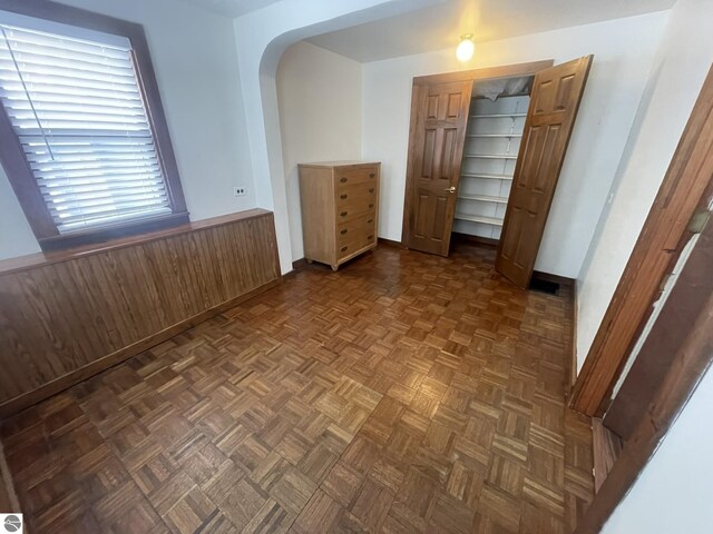 spare room featuring arched walkways, wooden walls, and wainscoting
