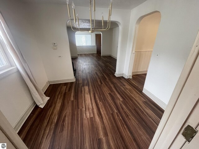 unfurnished dining area featuring arched walkways, baseboards, and wood finished floors