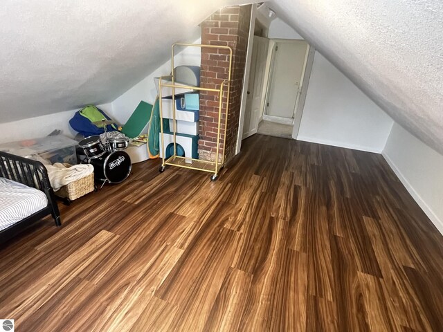 additional living space featuring baseboards, vaulted ceiling, wood finished floors, and a textured ceiling