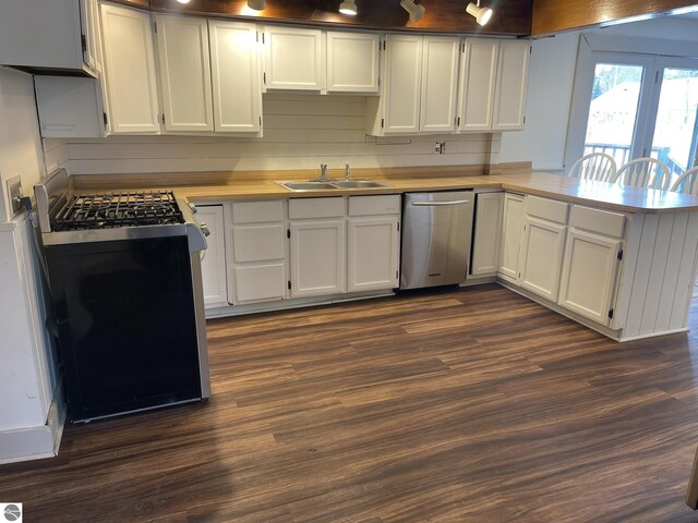kitchen featuring light countertops, a peninsula, appliances with stainless steel finishes, a sink, and dark wood-style floors