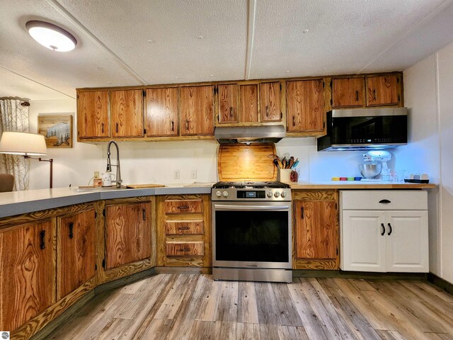 8468 Shorewood Ct, Mancelona, MI 49659 - kitchen featuring brown cabinetry, stainless steel range with gas cooktop, under cabinet range hood, and a sink