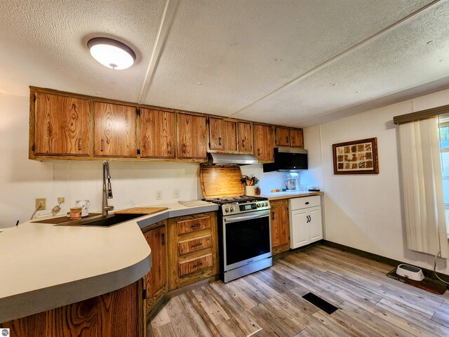 8468 Shorewood Ct, Mancelona, MI 49659 - kitchen featuring under cabinet range hood, stainless steel gas stove, a sink, light wood finished floors, and brown cabinets