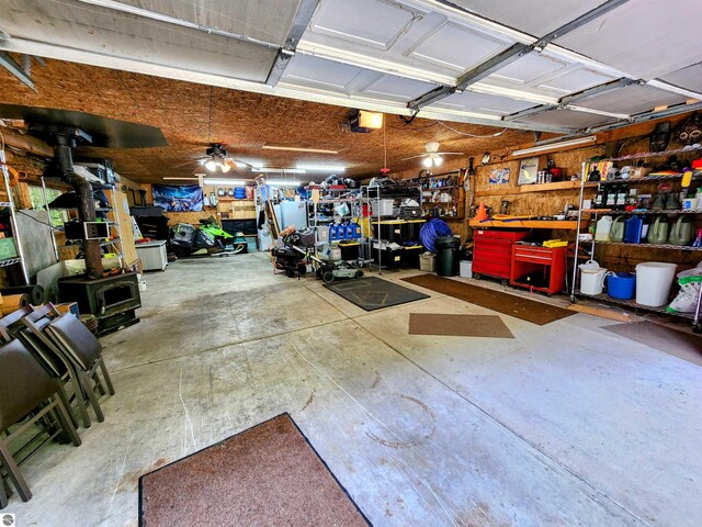 8468 Shorewood Ct, Mancelona, MI 49659 - garage featuring a workshop area, ceiling fan, a wood stove, and a garage door opener