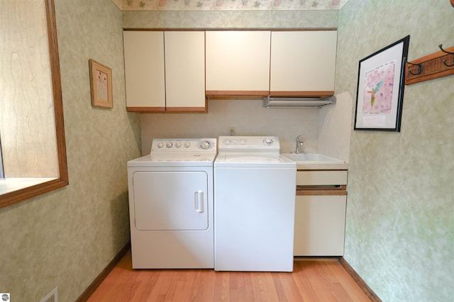 clothes washing area with a sink, light wood-type flooring, baseboards, separate washer and dryer, and cabinet space