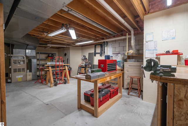 basement with concrete block wall, a workshop area, and heating unit