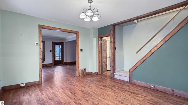 empty room with an inviting chandelier, baseboards, stairs, and wood finished floors