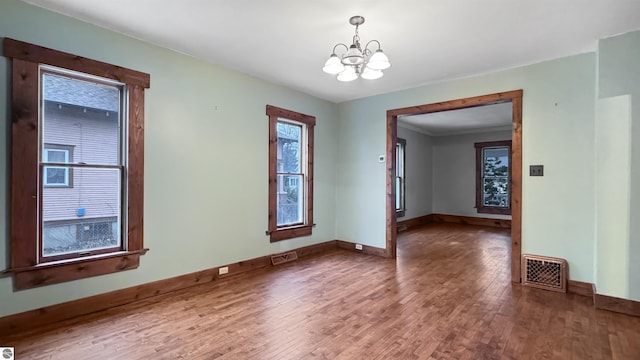 unfurnished room with baseboards, visible vents, a chandelier, and wood finished floors