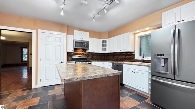 kitchen with decorative backsplash, appliances with stainless steel finishes, white cabinetry, a sink, and stone tile floors