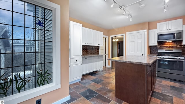 kitchen featuring white cabinetry, backsplash, stone tile flooring, and appliances with stainless steel finishes