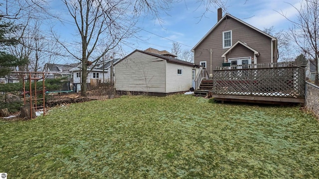 rear view of property with a wooden deck, a chimney, a trampoline, and a lawn