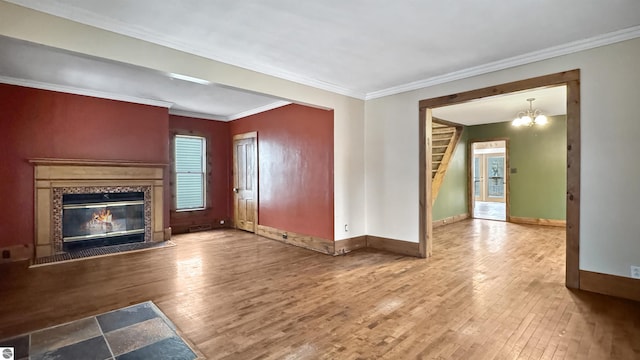 unfurnished living room with crown molding, wood finished floors, a glass covered fireplace, baseboards, and an inviting chandelier