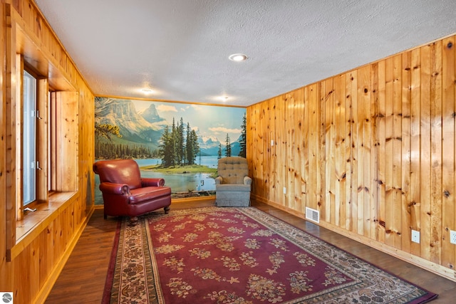 sitting room featuring visible vents, a textured ceiling, wood finished floors, and wood walls
