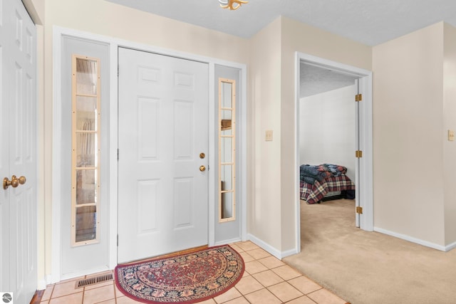 entrance foyer featuring baseboards, visible vents, light tile patterned floors, and light colored carpet