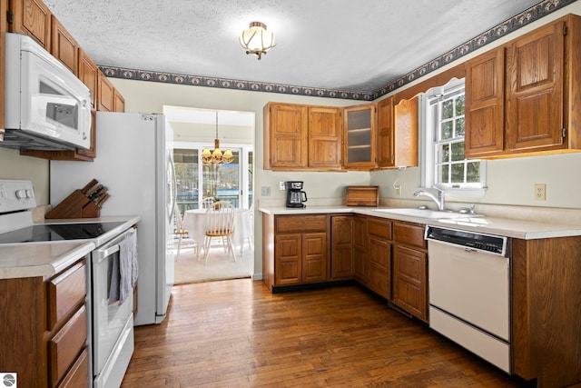 kitchen featuring an inviting chandelier, dark wood finished floors, brown cabinetry, and white appliances