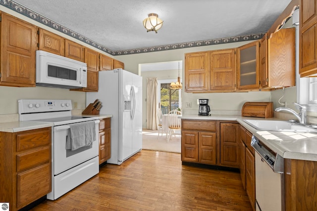 kitchen with light countertops, a sink, dark wood finished floors, brown cabinets, and white appliances