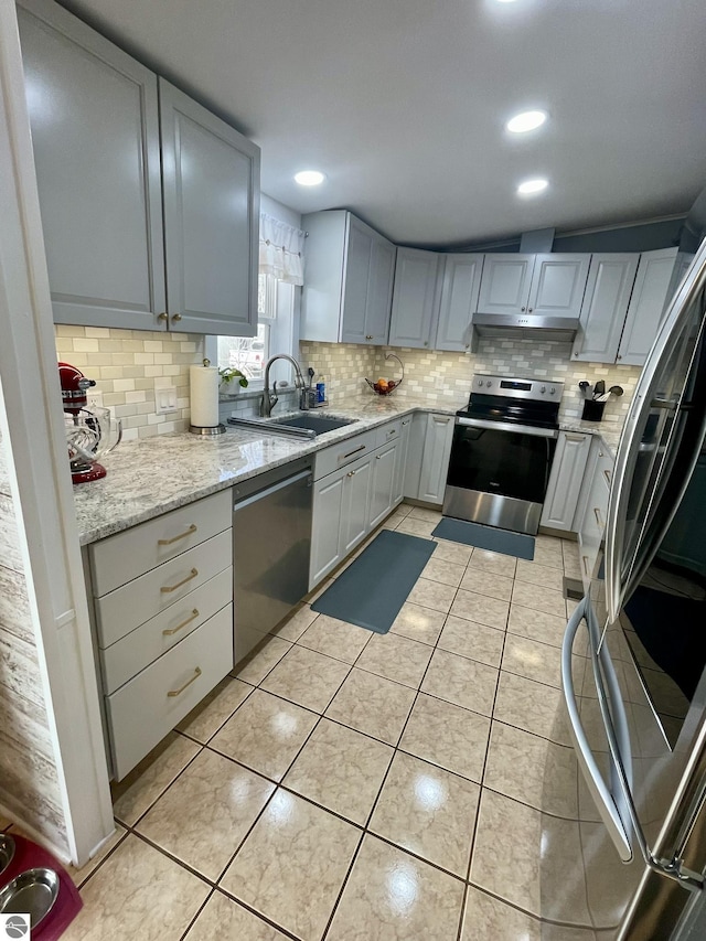 kitchen featuring appliances with stainless steel finishes, decorative backsplash, a sink, under cabinet range hood, and light tile patterned flooring