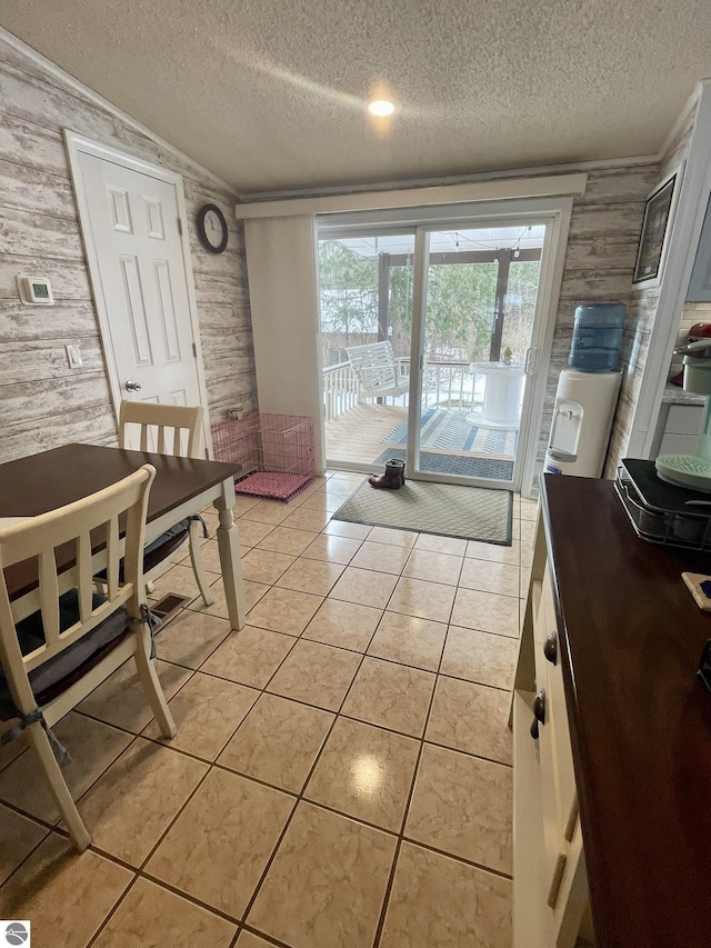 dining room featuring wood walls, a textured ceiling, wallpapered walls, and light tile patterned floors