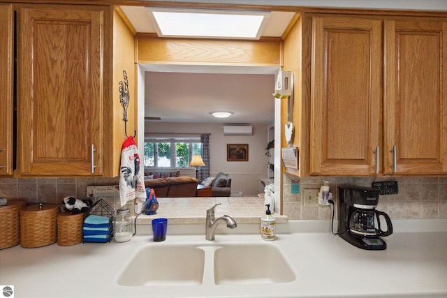 kitchen featuring light countertops, brown cabinetry, an AC wall unit, a sink, and backsplash