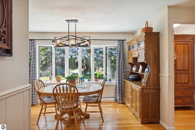 dining space with a wainscoted wall, light wood-style flooring, ornamental molding, and an inviting chandelier