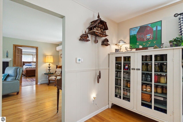 hall with a wainscoted wall, ornamental molding, baseboard heating, and wood finished floors