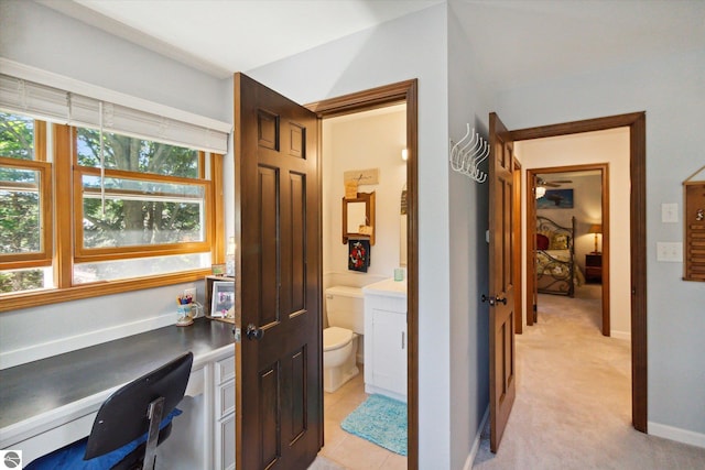 home office featuring baseboards, built in desk, and light carpet