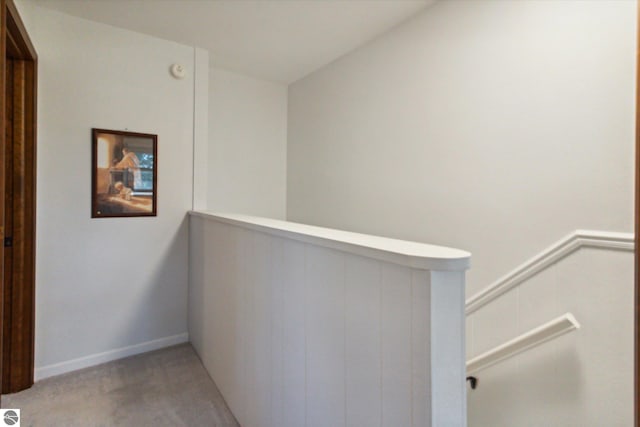 corridor with light colored carpet and an upstairs landing
