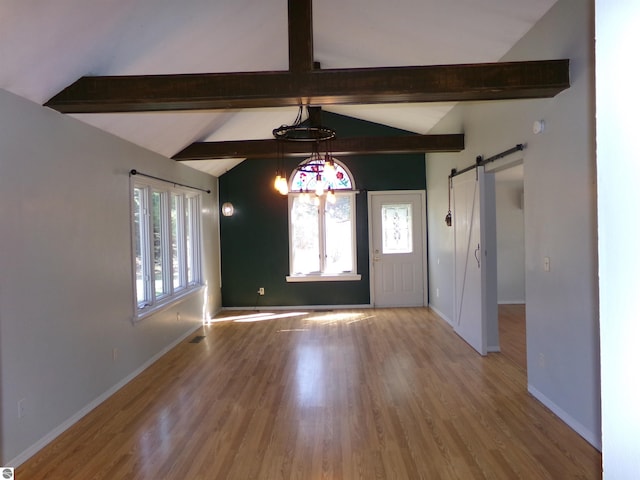 spare room featuring a barn door, wood finished floors, vaulted ceiling with beams, and baseboards