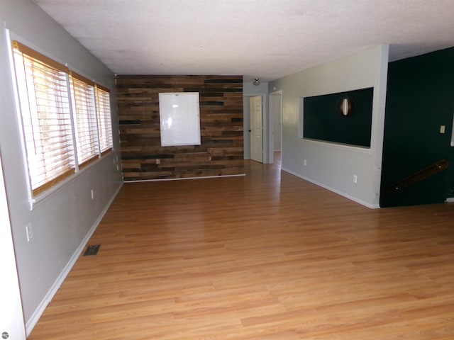 unfurnished living room featuring wood walls, baseboards, light wood finished floors, and visible vents