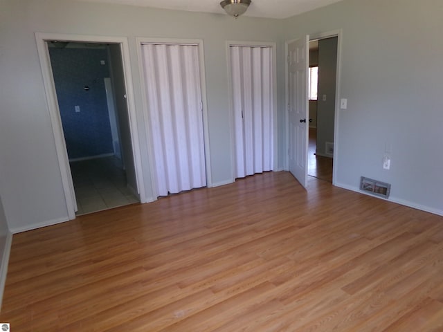 unfurnished bedroom with baseboards, multiple closets, visible vents, and light wood-type flooring