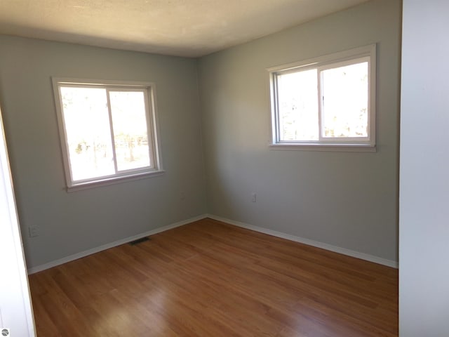 empty room with a wealth of natural light, wood finished floors, visible vents, and baseboards
