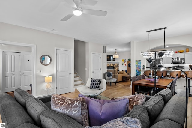 living area featuring light wood-type flooring, ceiling fan, stairs, and baseboards