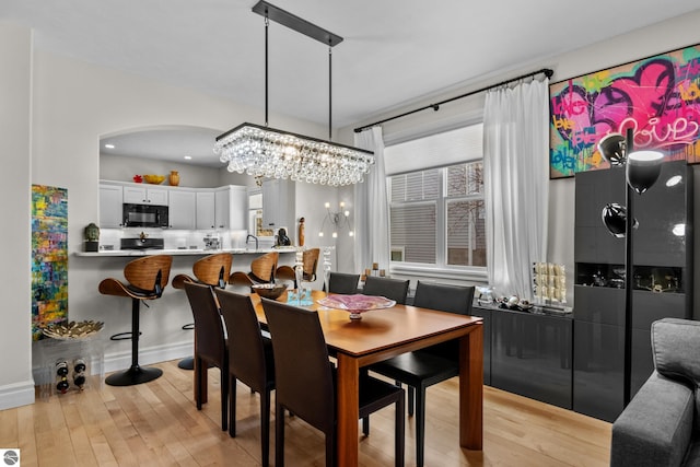 dining space featuring a chandelier, light wood-type flooring, arched walkways, and baseboards