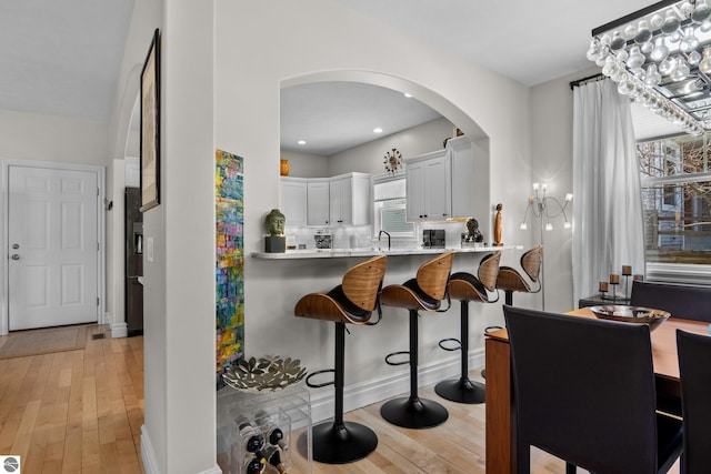 kitchen featuring arched walkways, light countertops, a breakfast bar, white cabinets, and light wood-style flooring