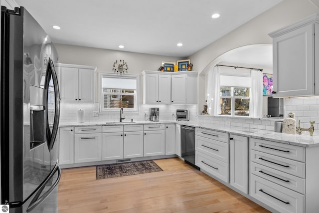 kitchen featuring appliances with stainless steel finishes, a sink, white cabinetry, tasteful backsplash, and arched walkways